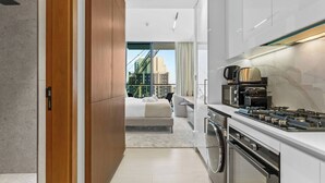 A modern kitchen with a gas stove, oven, and microwave. There is a balcony with a bed and a view of the city. - Minimalist Studio in Binghatti Azure (Jumeirah Village Circle (JVC))