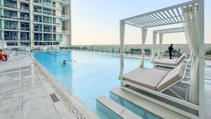A rooftop swimming pool with lounge chairs and a pergola. - Minimalist Studio in Binghatti Azure (Jumeirah Village Circle (JVC))