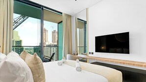 A hotel room with a large bed, a TV mounted on the wall, and a view of the cityscape through large windows. - Minimalist Studio in Binghatti Azure (Jumeirah Village Circle (JVC))