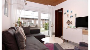 Un soggiorno moderno con un divano grigio, un tavolino da caffè bianco e una TV a schermo piatto su un mobile bianco.