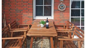 Un tavolo di legno con due bicchieri da vino e una bottiglia, circondato da sedie di legno, di fronte a un muro di mattoni con una finestra e un cartello decorativo.