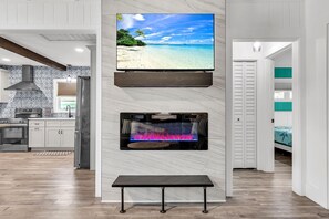 A modern kitchen with white cabinets, a built-in stove, and a large flat-screen TV mounted above a fireplace. - Rocking Sunset Beach House (Treasure Island)