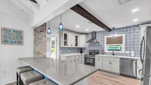 A modern kitchen with a central island, white cabinets, a brick accent wall, and a patterned backsplash. - Rocking Sunset Beach House (Treasure Island)