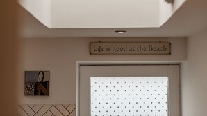 Um quarto com uma luminária no teto, uma placa na parede com a frase 'Life is good at the Beach' e uma obra de arte emoldurada com a letra 'N'.