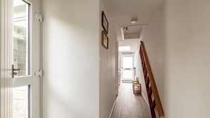 Um corredor estreito com piso de madeira, paredes brancas e uma escada de madeira à direita.