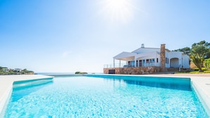A modern house with a swimming pool, stone walls, and a view of the ocean. - Can Ferrando House with Sea Views, Wi-Fi and Air Conditioning (Cala Santanyi - Santanyi)