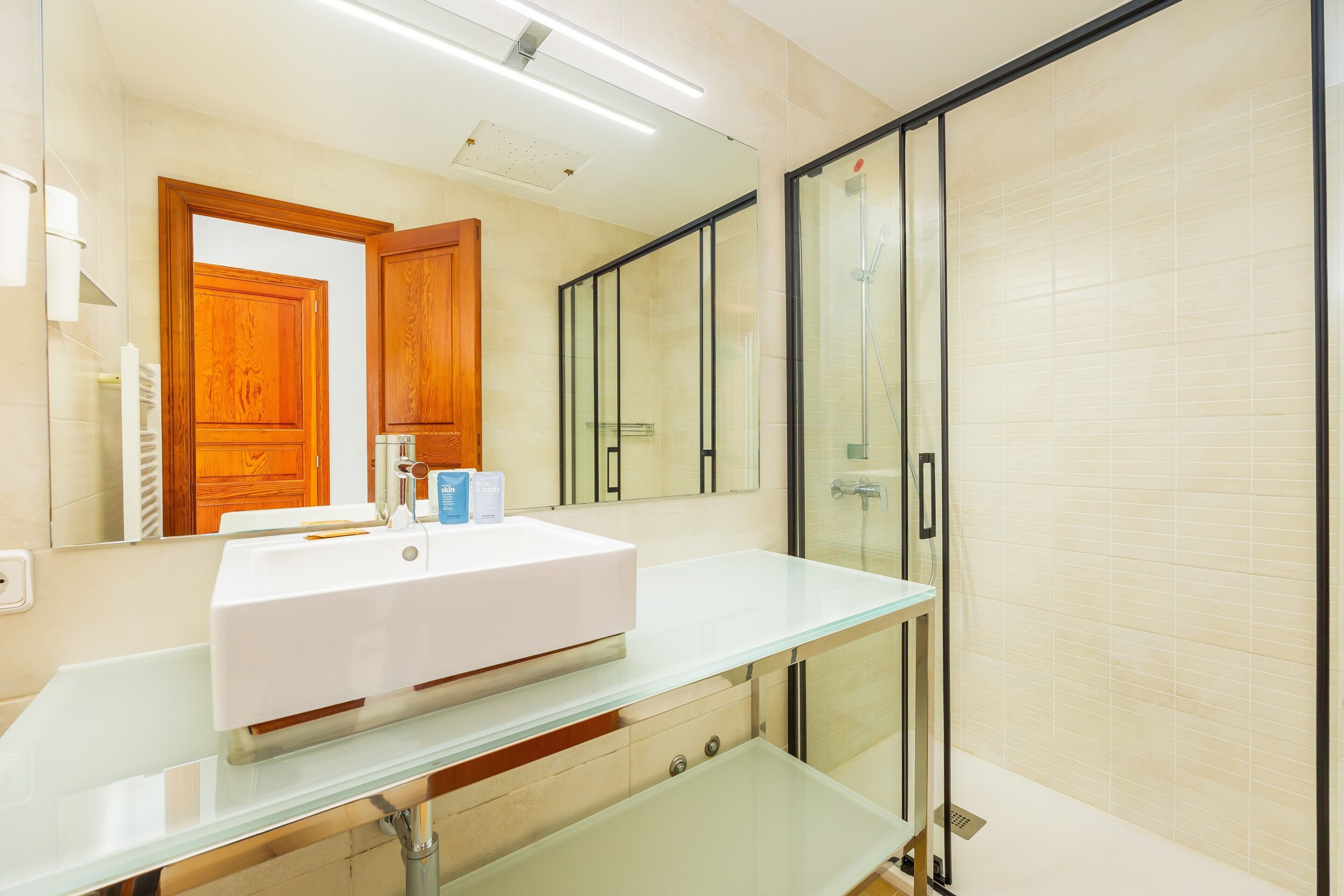 A modern bathroom with a glass vanity, a large mirror, a shower enclosure, and wooden cabinets.