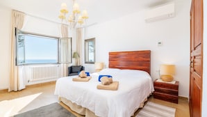 A bedroom with a large bed, a wooden headboard, a nightstand, a lamp, a window with a view, and a radiator. - Can Ferrando House with Sea Views, Wi-Fi and Air Conditioning (Cala Santanyi - Santanyi)