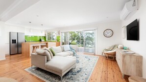 En moderne stue med sofa, spiseplads og køkken med grønne detaljer.