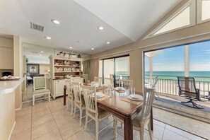 Un comedor amplio con una mesa grande dispuesta para seis personas, una zona de cocina con bufé, y un balcón con vista al océano.