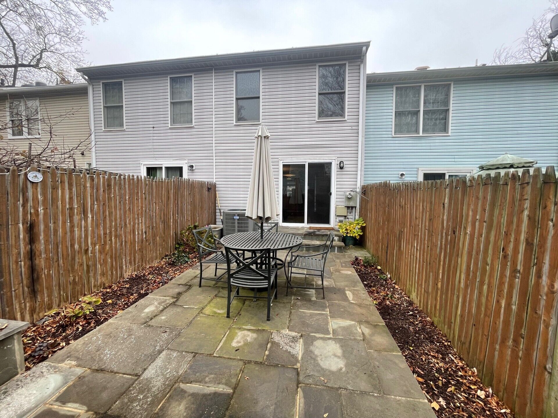 A patio area with a table and chairs, a sliding glass door, and a wooden fence.