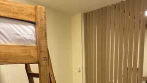 Uma cama beliche com estrutura de madeira, um cobertor azul e uma cesta de palha no chão.