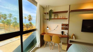 Una habitación moderna con escritorio, dos sillas, televisión y vista a la playa.
