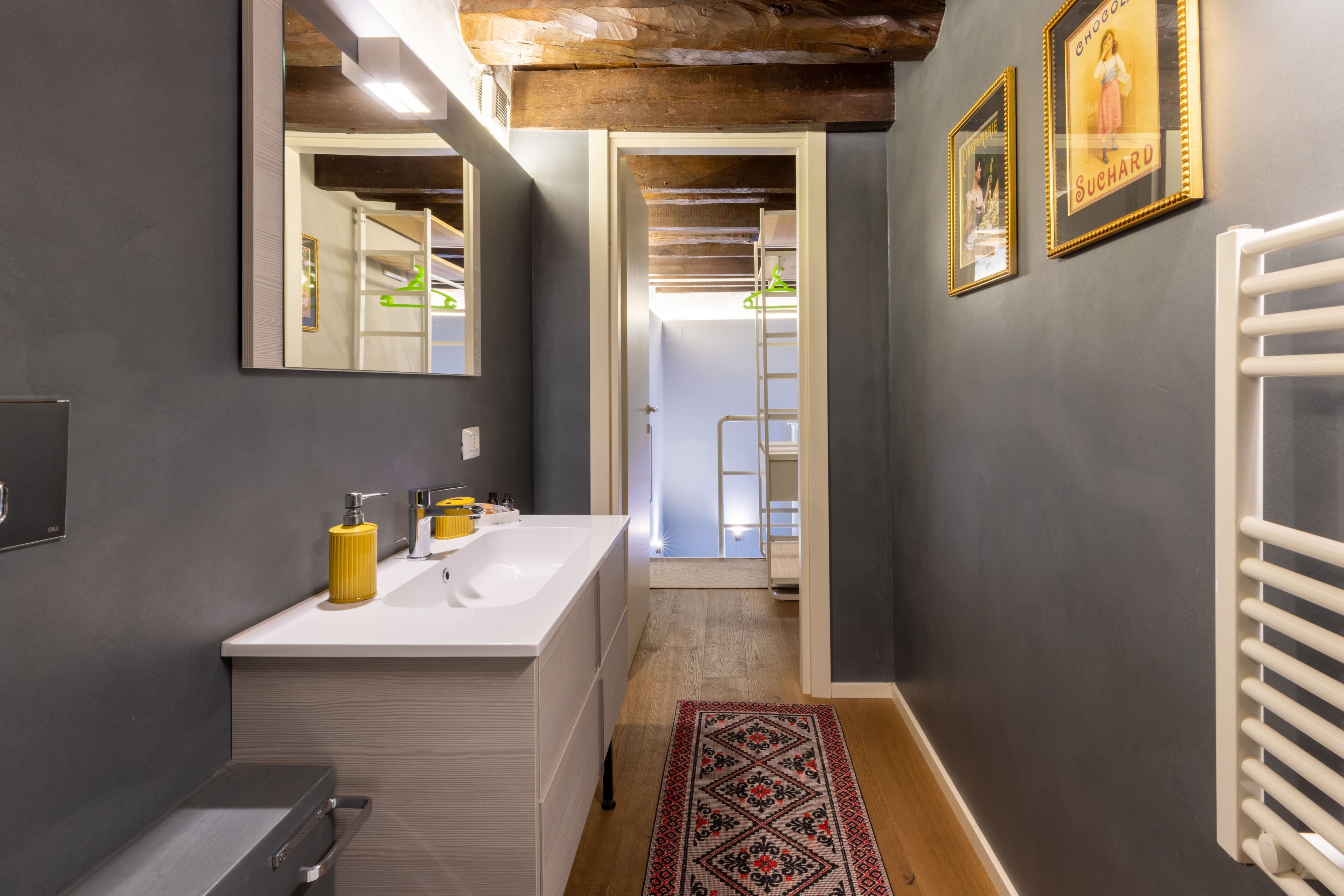 A modern bathroom with a large mirror, a white sink, and a wooden floor.