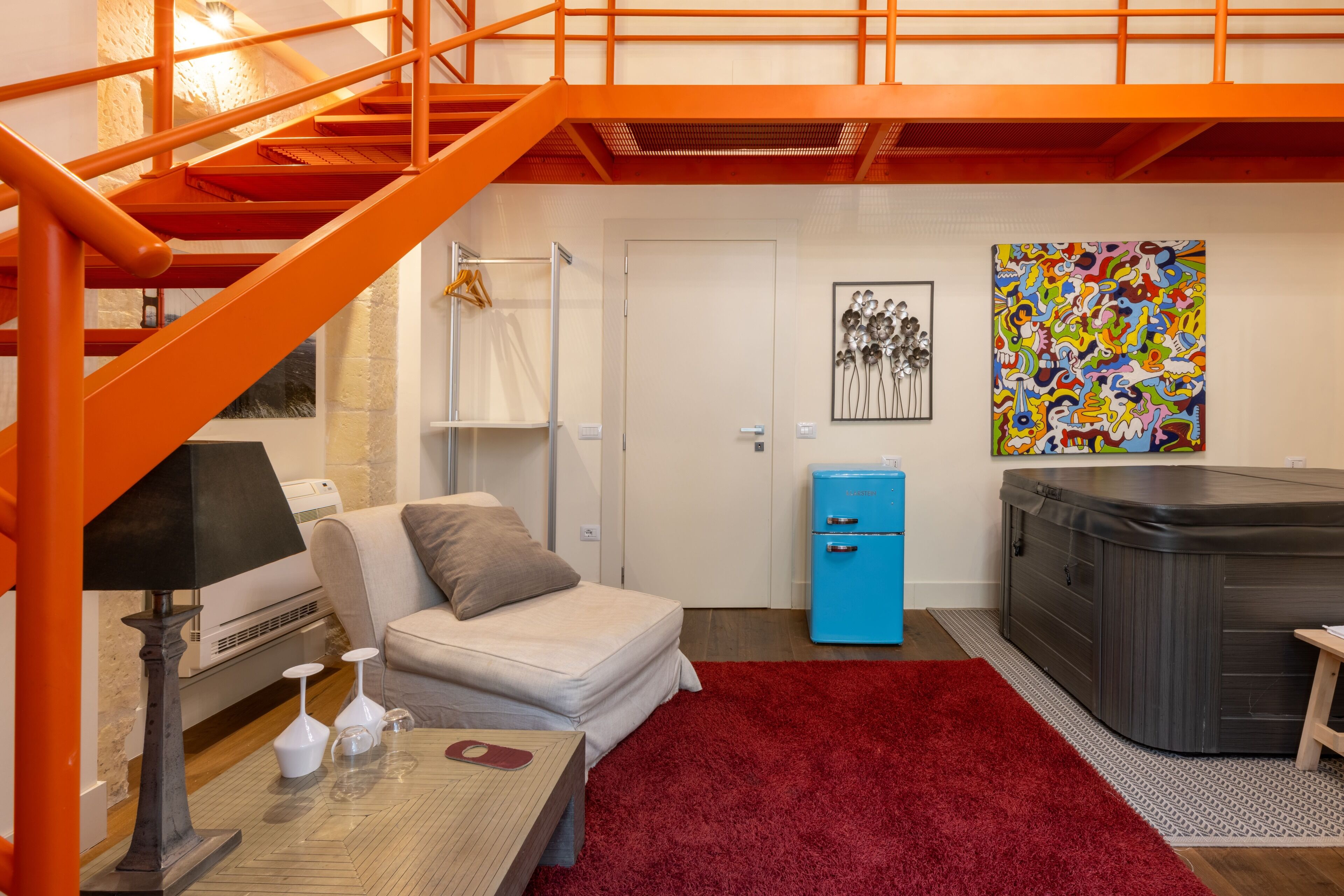 A room with a red carpet, a sofa, a small table with a lamp, a blue cabinet, and a hot tub.