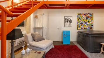 A room with a red carpet, a sofa, a small table with a lamp, a blue cabinet, and a hot tub.