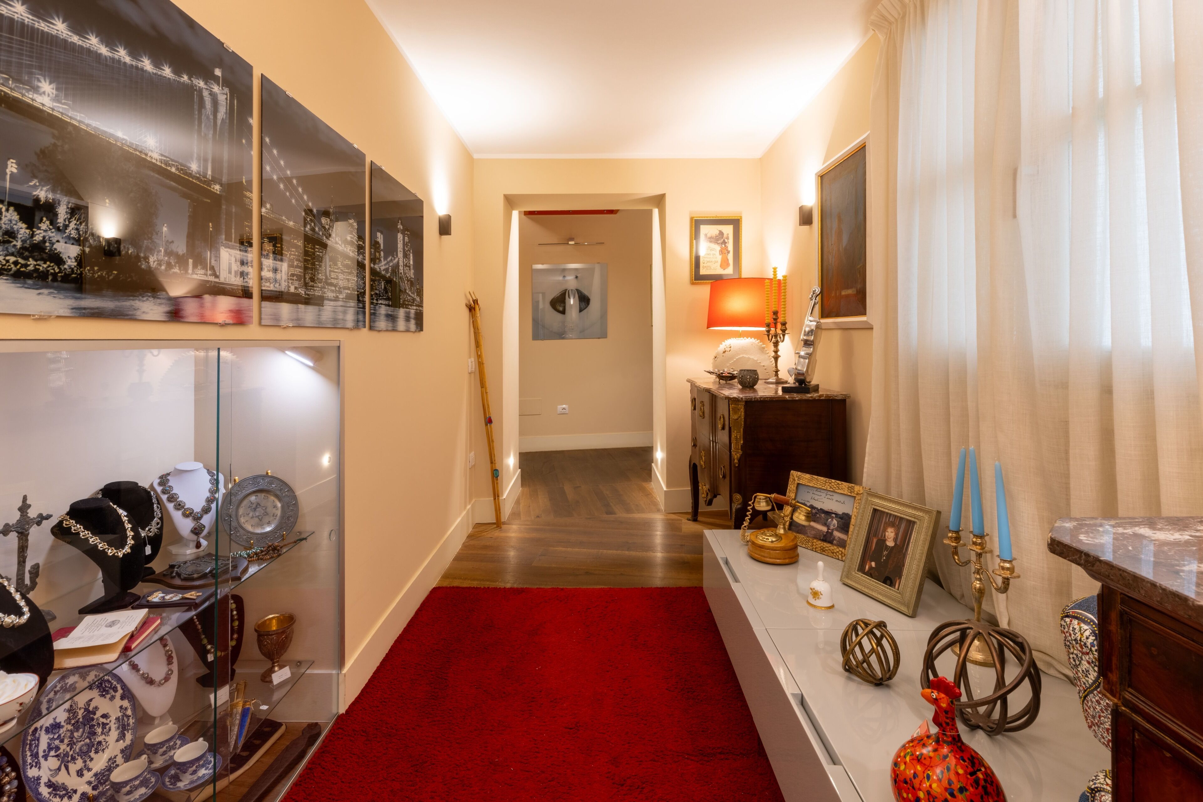 Un pasillo con alfombra roja, una vitrina de vidrio con joyería, piso de madera y una puerta que da a otra habitación.