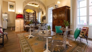 A spacious living area with a large wooden cabinet, a round table, and clear chairs. - Hotiday Cagliari Porto (Cagliari)