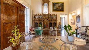 A room with a wooden door, a large mirror, a religious icon, a dining table with chairs, and a patterned rug. - Hotiday Cagliari Porto (Cagliari)