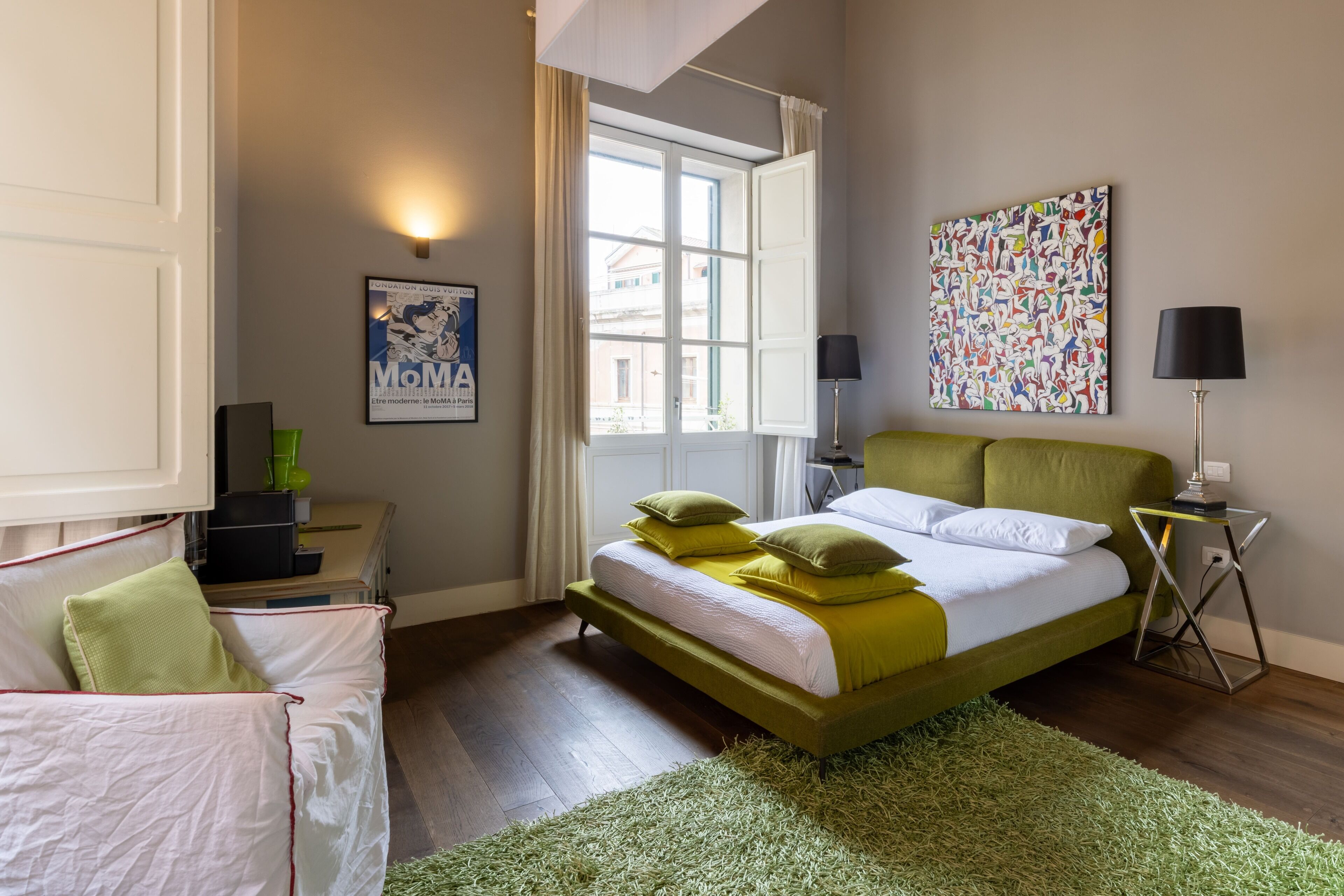 Un dormitorio moderno con una cama verde, ropa de cama blanca, una alfombra verde, una mesita de noche con una lámpara y un cartel en la pared.