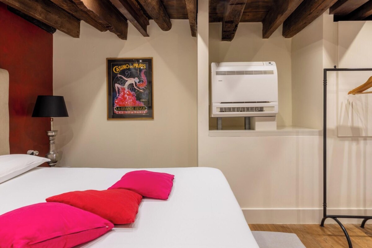 A hotel room with a bed, a poster on the wall, an air conditioning unit, and a wooden ceiling.