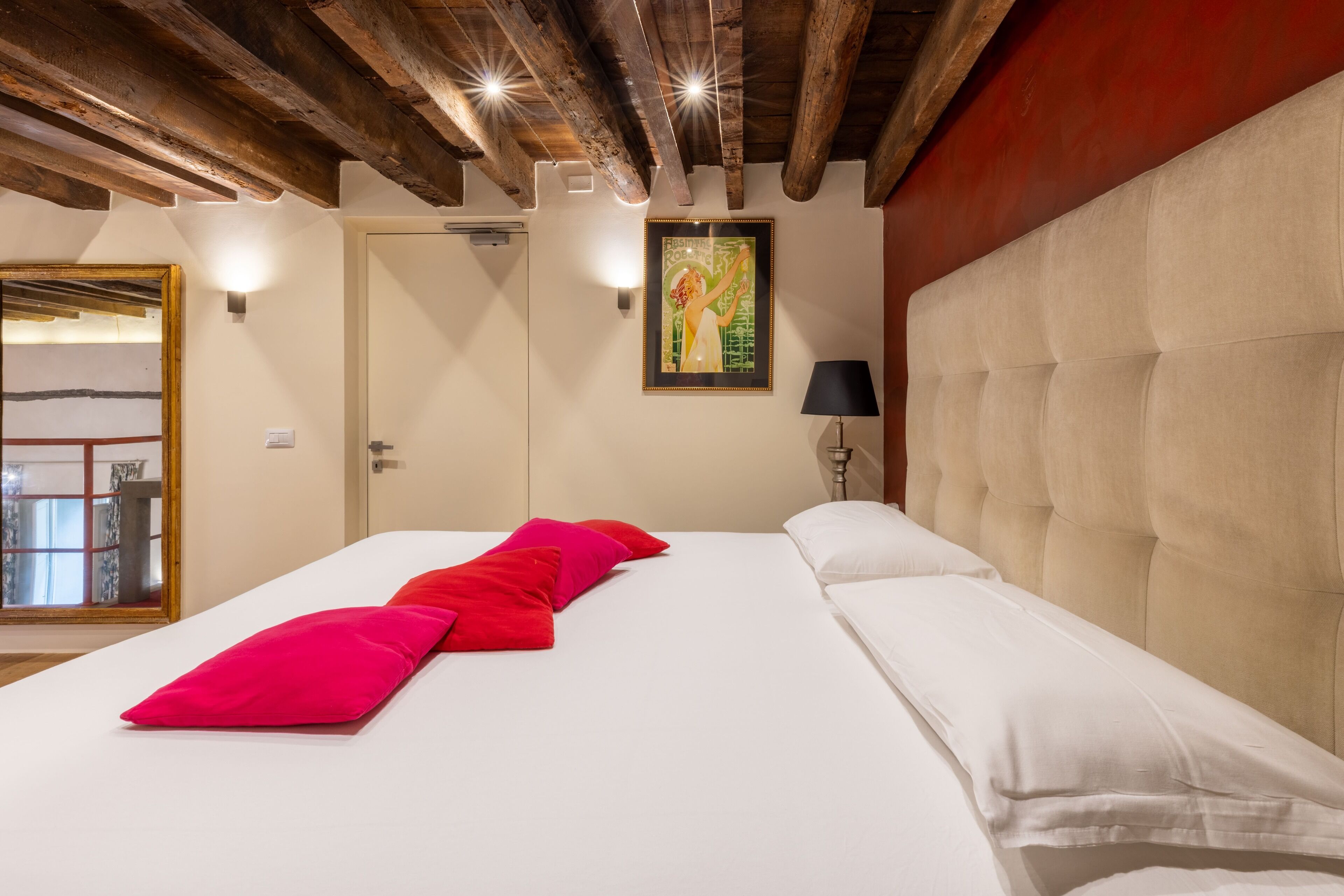 Ein Hotelzimmer mit einem großen Bett, einer Holzbalkendecke, einem Gemälde an der Wand und einer Lampe.