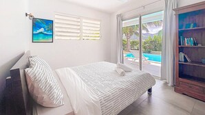 Slaapkamer met een bed, een plafondventilator, een raam met zonwering, een boekenkast en uitzicht op een zwembad.