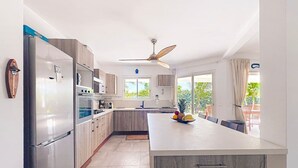 Een moderne keuken met een groot kookeiland, roestvrijstalen apparatuur en een plafondventilator.