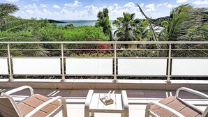 Een balkon met uitzicht op zee, omgeven door groen en palmbomen.