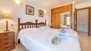 A bedroom with a wooden bed, two bedside tables, a nightstand, a mirror, and a door leading to another room. - Holiday Home 'Sa Trona' with Sea Views, Private Terrace and Wi-Fi (Cala Santanyi - Santanyi)