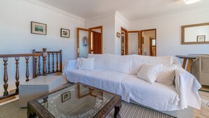 A white sofa, a glass coffee table, and a wooden railing in a room with white walls and a ceiling light. - Holiday Home 'Sa Trona' with Sea Views, Private Terrace and Wi-Fi (Cala Santanyi - Santanyi)
