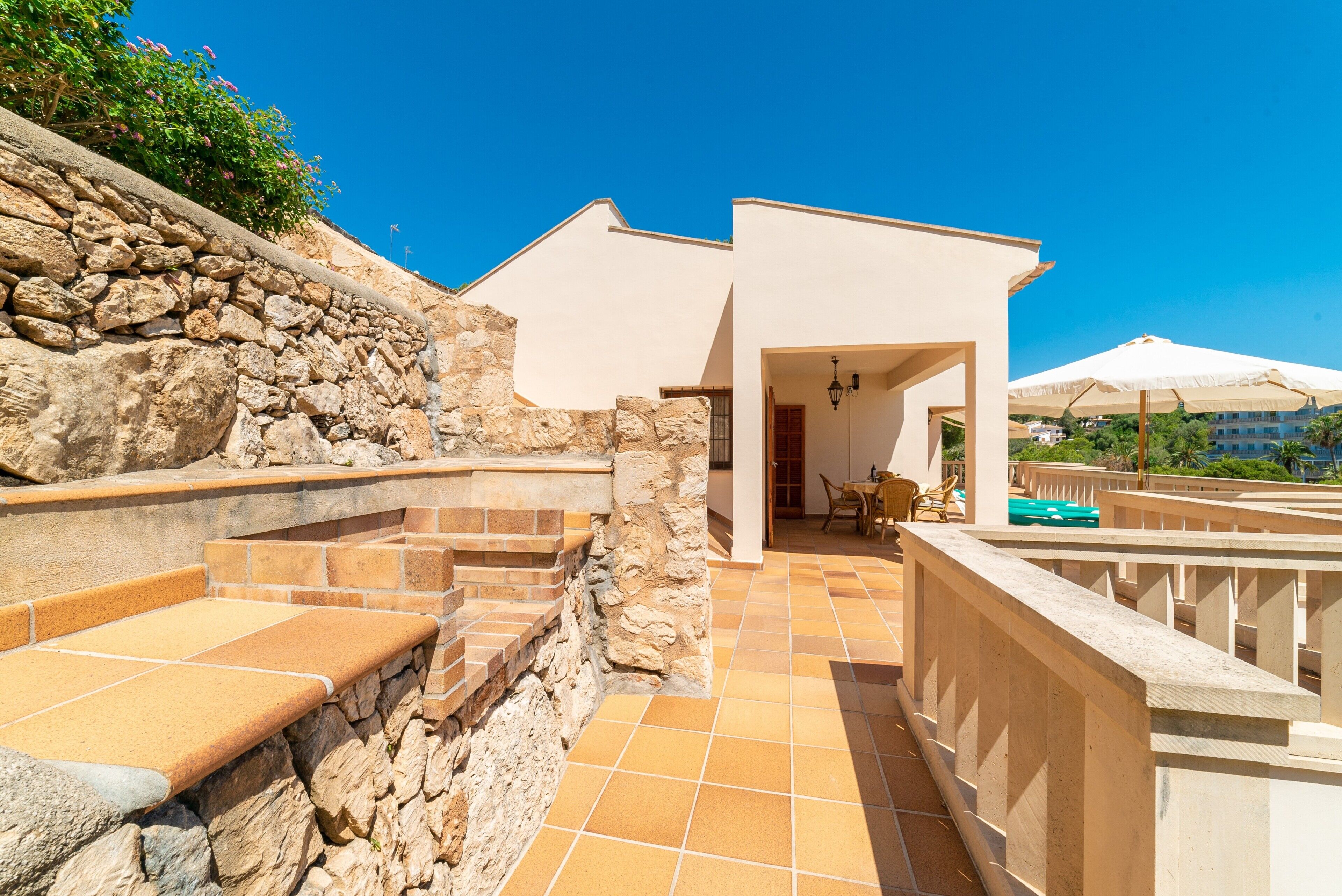 Un muro de piedra, un patio con escalones, la entrada de un edificio y mobiliario exterior.