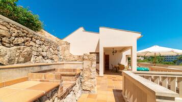 Un muro de piedra, un patio con escalones, la entrada de un edificio y mobiliario exterior.