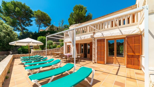 A poolside area with sun loungers, a covered seating area, and a building with wooden shutters. - Holiday Home 'Sa Trona' with Sea Views, Private Terrace and Wi-Fi (Cala Santanyi - Santanyi)