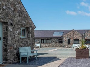 A stone building with a bench, a small garden, and a paved area. - Blue Bird Cottage (Gaerwen)