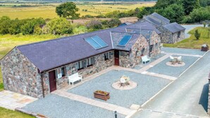 A stone building with a sloped roof, solar panels, and outdoor seating areas. - Blue Bird Cottage (Gaerwen)