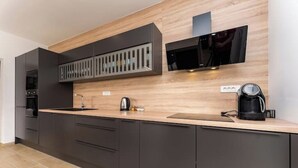 A modern kitchen with dark cabinetry, a wooden countertop, a built-in microwave, and a coffee maker. - Villa Cissa (Stara Novalja)