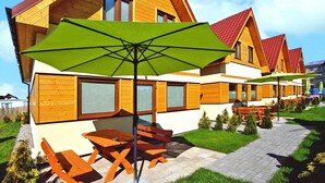 A row of wooden cabins with a patio area, outdoor seating, and a green umbrella. - Spacious holiday homes with terraces, Sarbinowo (Sarbinowo)