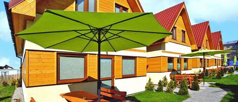Una fila de cabañas de madera con un espacio de patio, asientos exteriores y una sombrilla verde.