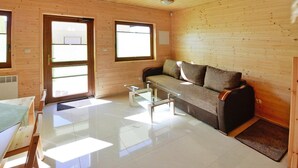 A wooden cabin interior with a sofa, a glass coffee table, and a door with a window. - Spacious holiday homes with terraces, Sarbinowo (Sarbinowo)