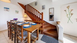 Ein Essbereich mit einem Holztisch, gedeckt für vier Personen, einer Treppe und einer Tür mit einem Blumenbild.