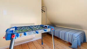Ein Zimmer mit einem Tischkicker, einem Bett mit blauer Streifenoptik und einem Metallgitter.