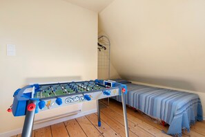 A room with a foosball table, a bed with a blue striped blanket, and a metal gate. - Holiday Home "Ty Gwen - Plouezoc'h" with Sea View and Wi-Fi (Plouezoc'h)