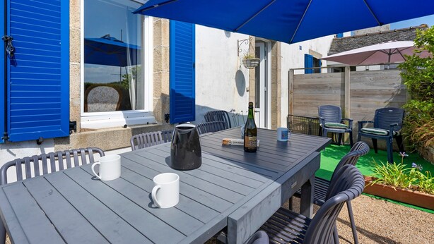 Eine Terrasse im Freien mit Tisch, Stühlen, einem blauen Sonnenschirm und einer Weinflasche.