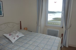 Een slaapkamer met een bed, een raam met gordijnen, een radiator en een aan de muur hangend schilderij.