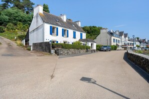 A street with white houses, a stone wall, and parked cars. - Holiday Home "Ty Gwen - Plouezoc'h" with Sea View and Wi-Fi (Plouezoc'h)