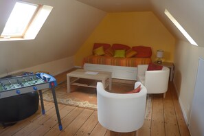 Een kamer met een tafelvoetbaltafel, een bank, een salontafel en een bed met kleurrijke kussens.