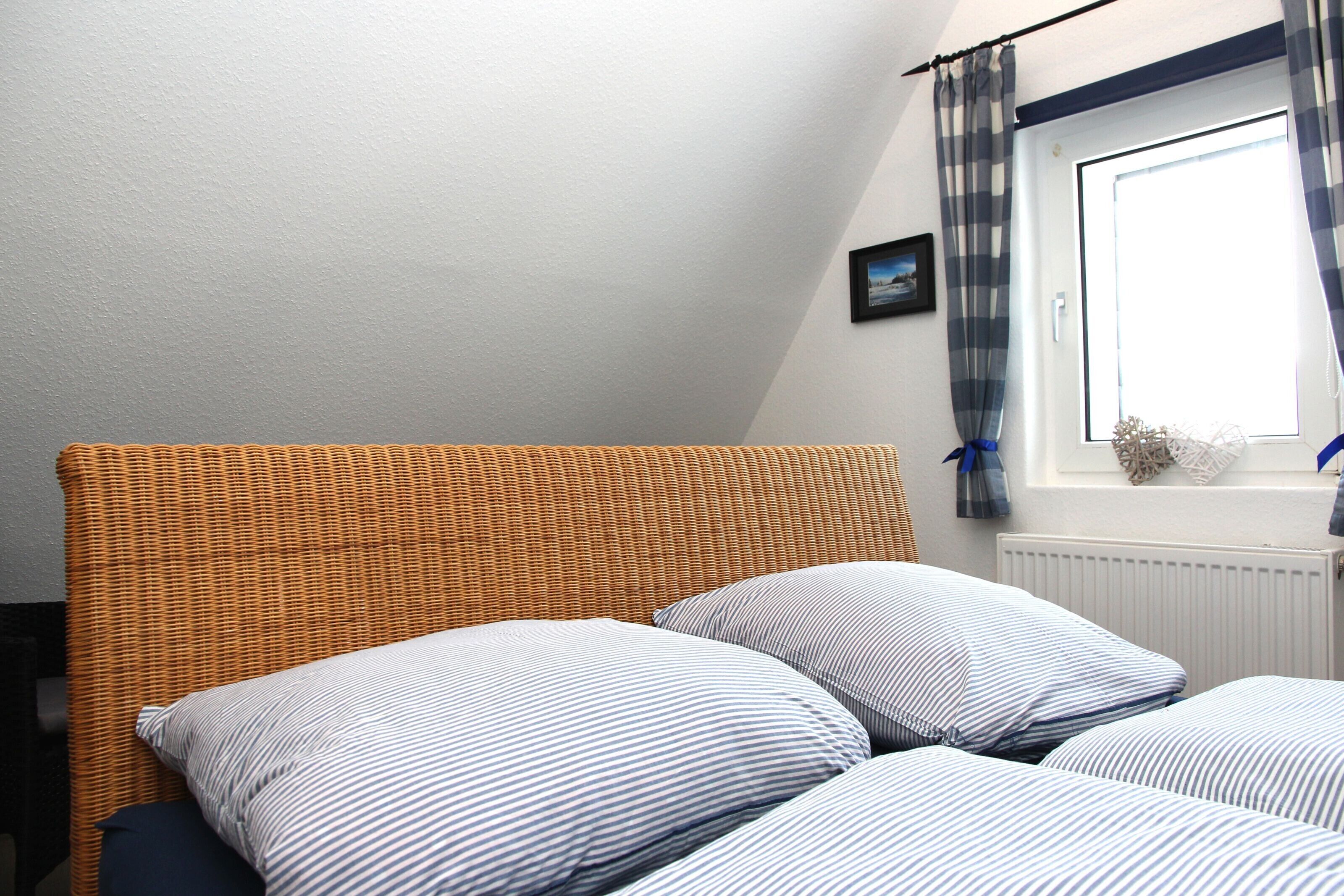 A bedroom with a bed, a window with curtains, and a picture on the wall.