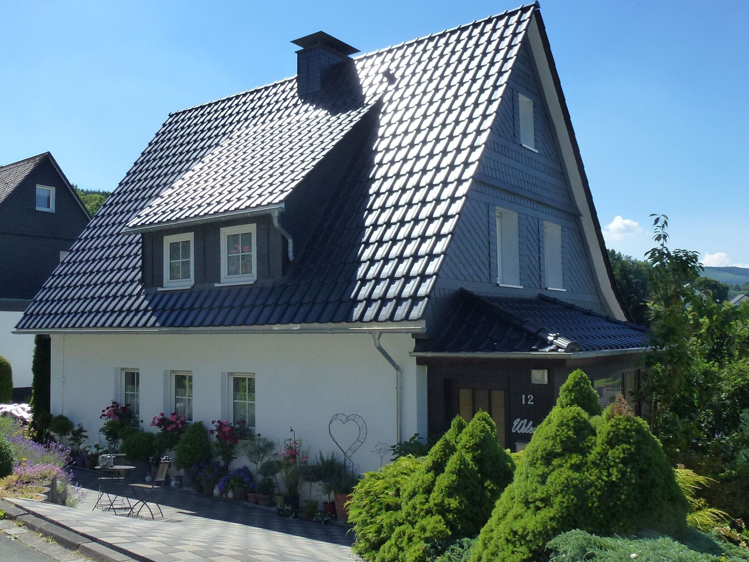 A house with a steeply pitched roof, a chimney, and a number '12' on the front door.