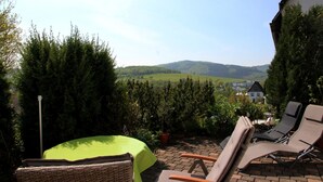 A patio with outdoor furniture, a table with a green tablecloth, and a view of a house and hills in the background. - Holiday Apartment “Olsberg” with Mountain View, Private Terrace and Wi-Fi (Olsberg)